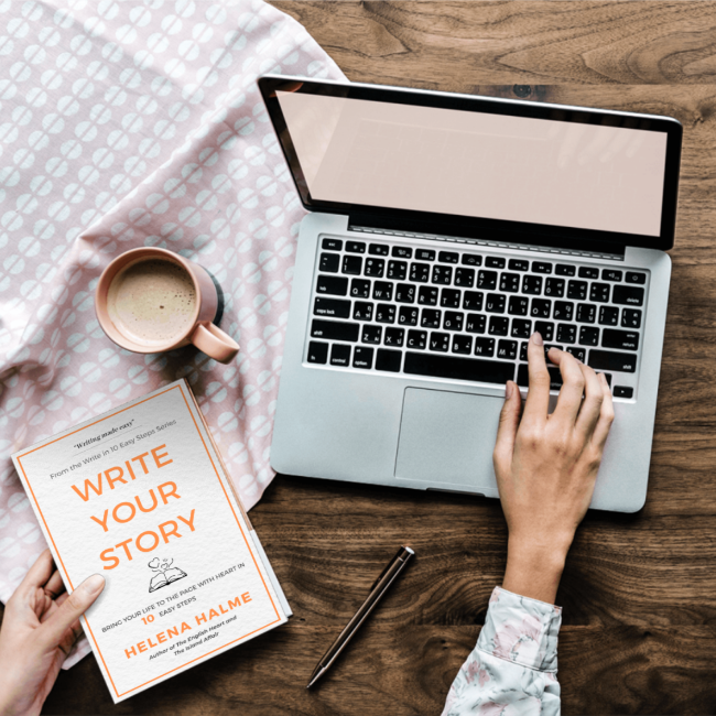 Person using a laptop with a book titled 'Write Your Story' on a wooden table.