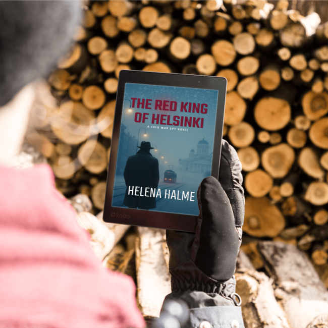 Person holding a tablet with 'The Red King of Helsinki' book cover against a wooden log background