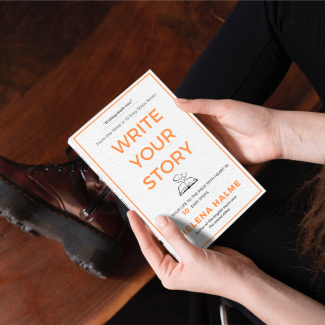 Person holding a book titled 'Write Your Story' by Elena Halme on a wooden floor.